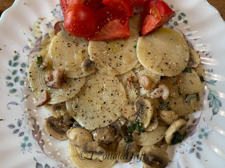 white plate with circular pasta, mushrooms, and bright red tomatoes